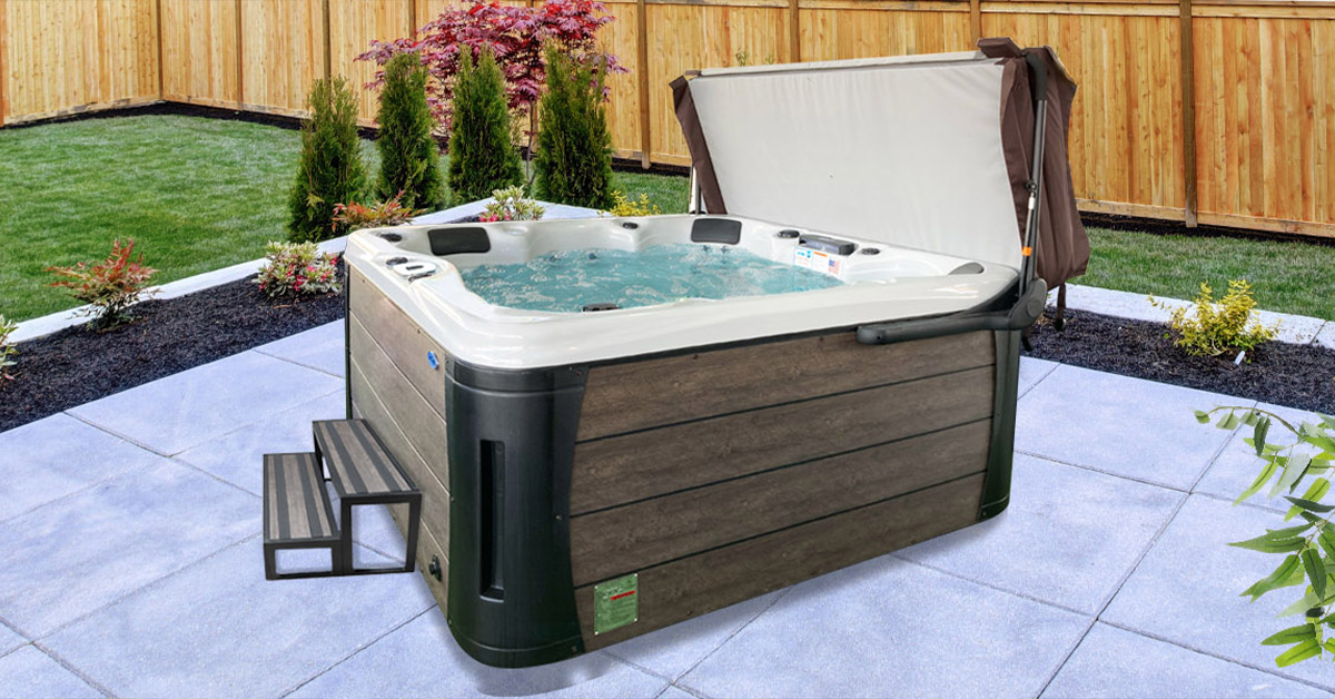 A hot tub with steps on a stone tile patio, with a spa cover raised on a cover lift